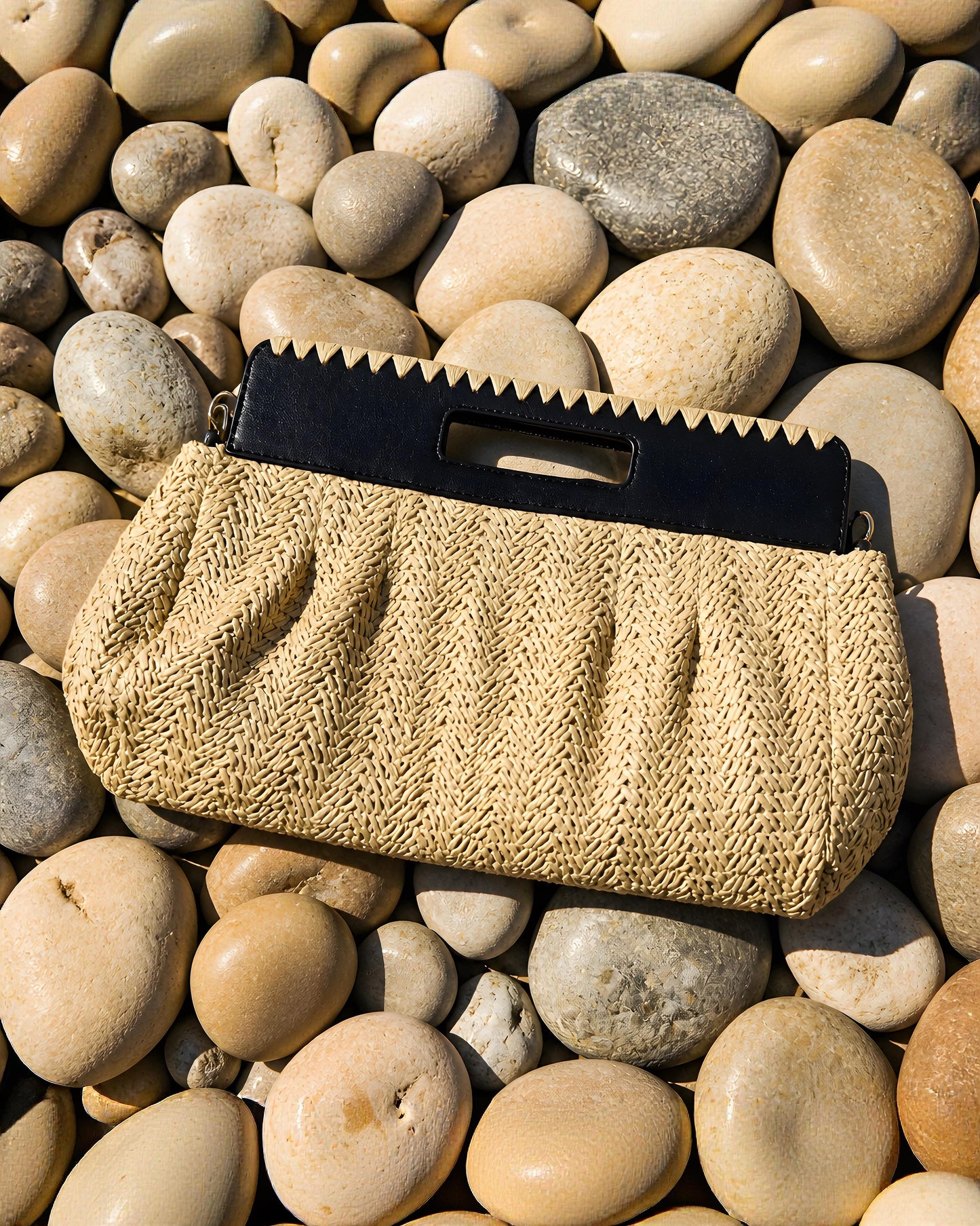 Bolso de mano tipo Clutch Besos de EUTEA, con cuerpo de paja de papel tejida en espiga color crema y una elegante asa de mano rígida troquelada en color negro.
