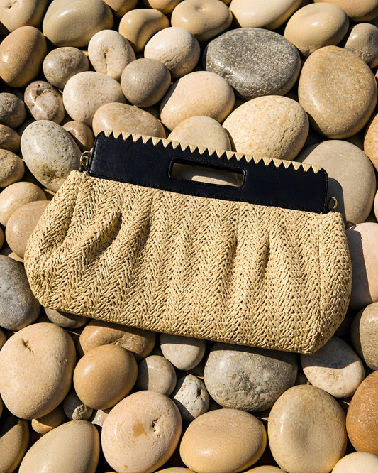 Bolso de mano tipo Clutch Besos de EUTEA, con cuerpo de paja de papel tejida en espiga color crema y una elegante asa de mano rígida troquelada en color negro.