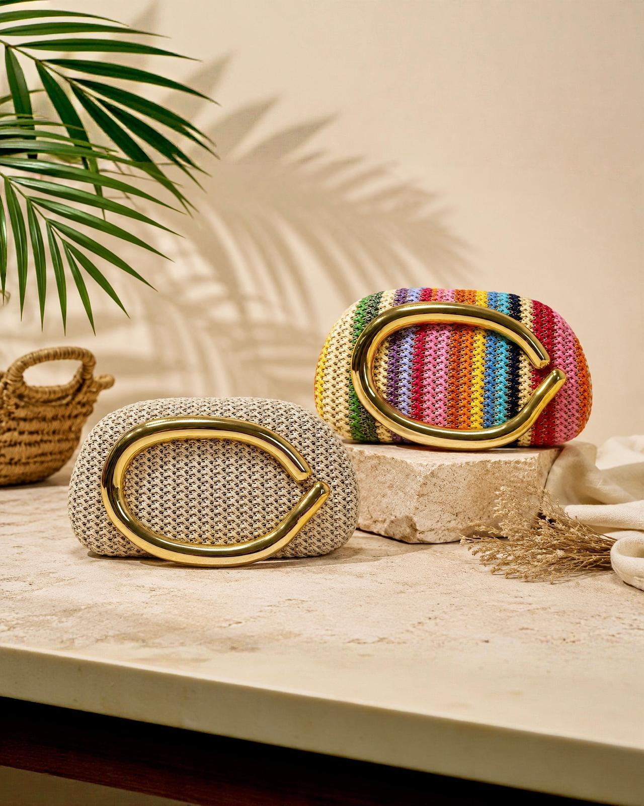 Bolso clutch rígido de tipo caja MarBella de EUTEA, revestido con paja de papel trenzada en un vibrante patrón de rayas verticales multicolor y rematado con un asa de mano metálica dorada de diseño curvo y escultural.