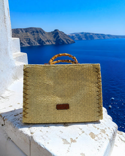Bolso de mano Gracia de EUTEA, un maletín estructurado de paja de papel en tono crema con costuras decorativas cruzadas en los bordes y asas superiores rígidas con diseño de efecto bambú.