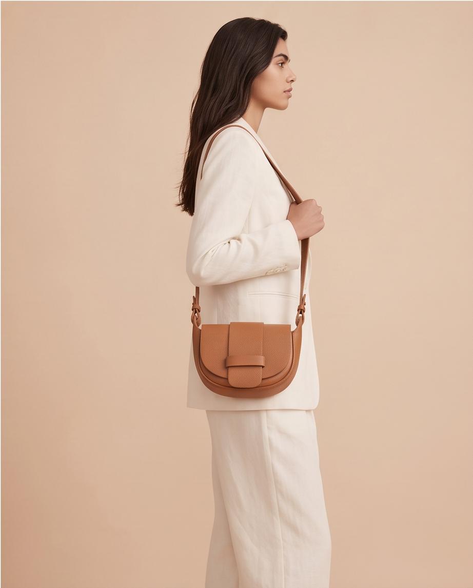 Modelo luciendo el bolso bandolera Malvarrosa en tono marrón camel combinado con un traje blanco.