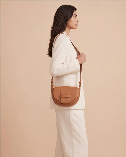 Modelo luciendo el bolso bandolera Malvarrosa en tono marrón camel combinado con un traje blanco.