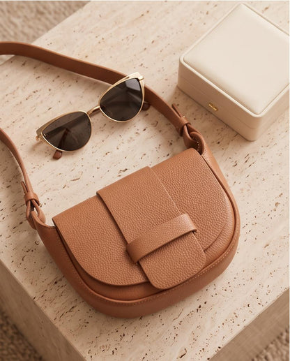 Plano cenital del bolso Malvarrosa en piel color camel junto a unas gafas de sol y un joyero.