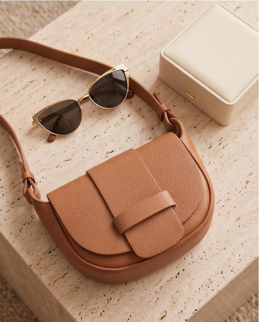 Plano cenital del bolso Malvarrosa en piel color camel junto a unas gafas de sol y un joyero.