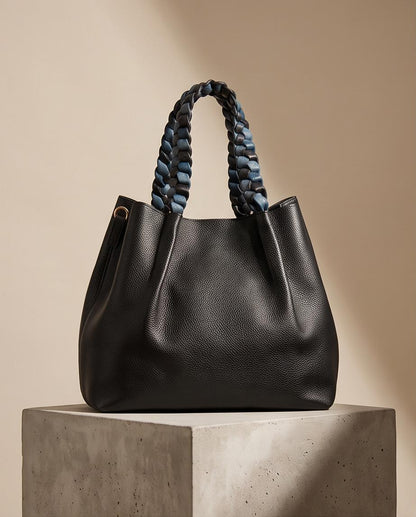 Bolso shopper de piel sintética negra Maristas sobre pedestal con asas trenzadas en azul y negro.