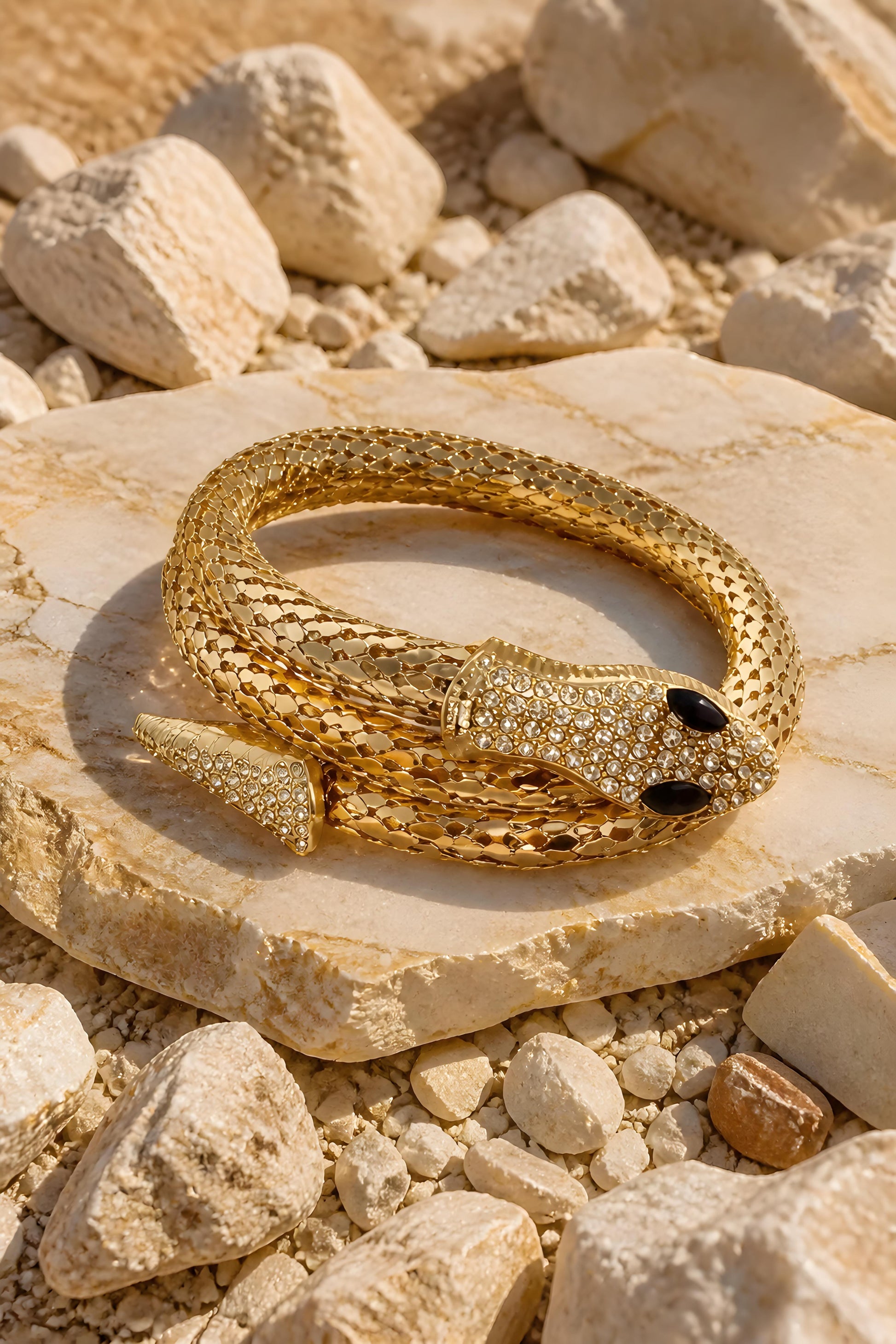 Brazalete dorado de serpiente Tossa con pavé de cristales brillantes expuesto sobre una piedra natural clara.