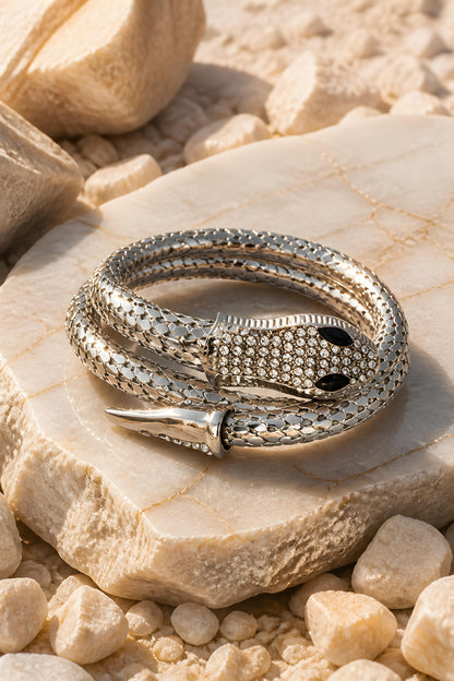 Brazalete plateado de serpiente flexible Tossa de EuTea, con cabeza y cola detalladas en cristales sobre fondo de rocas.