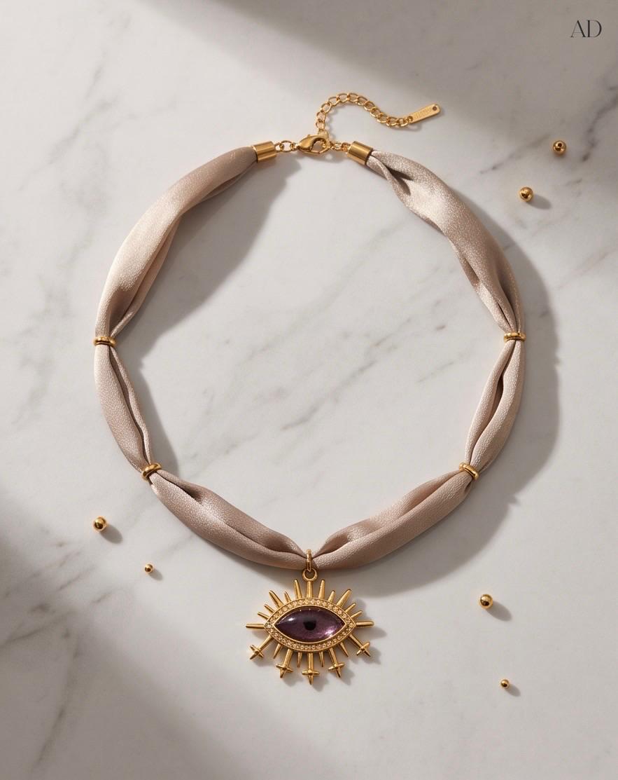 Collar Amuleto Ojo Violeta de tejido beige con colgante dorado y cadena extensora.