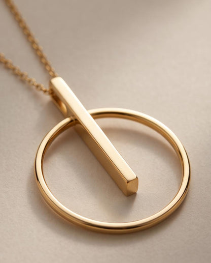 Detalle del Collar Calderería dorado de acero inoxidable con colgante geométrico de círculo y barra.