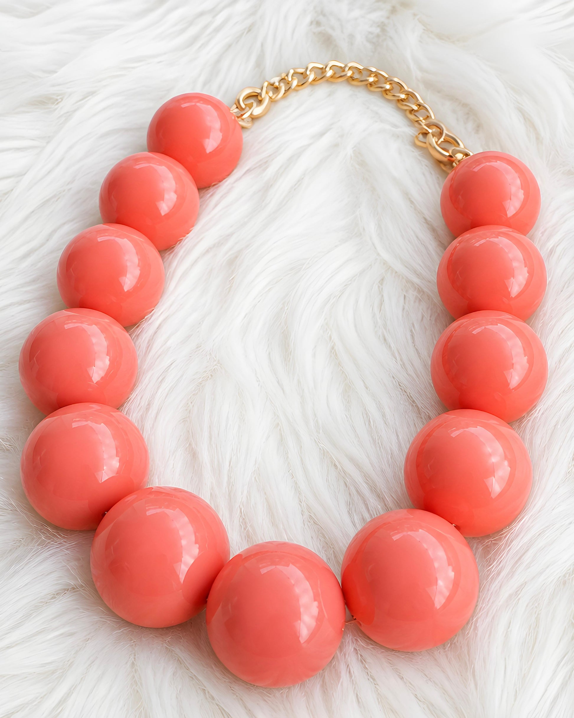 Collar de bolas grandes color coral brillante sobre fondo de pelo blanco