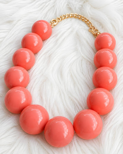 Collar de bolas grandes color coral brillante sobre fondo de pelo blanco