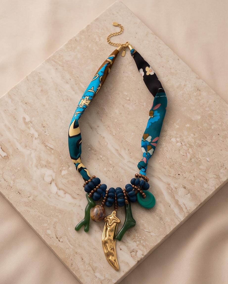 Collar Larios con tejido estampado, cuentas azules y colgantes decorativos sobre una superficie de piedra.