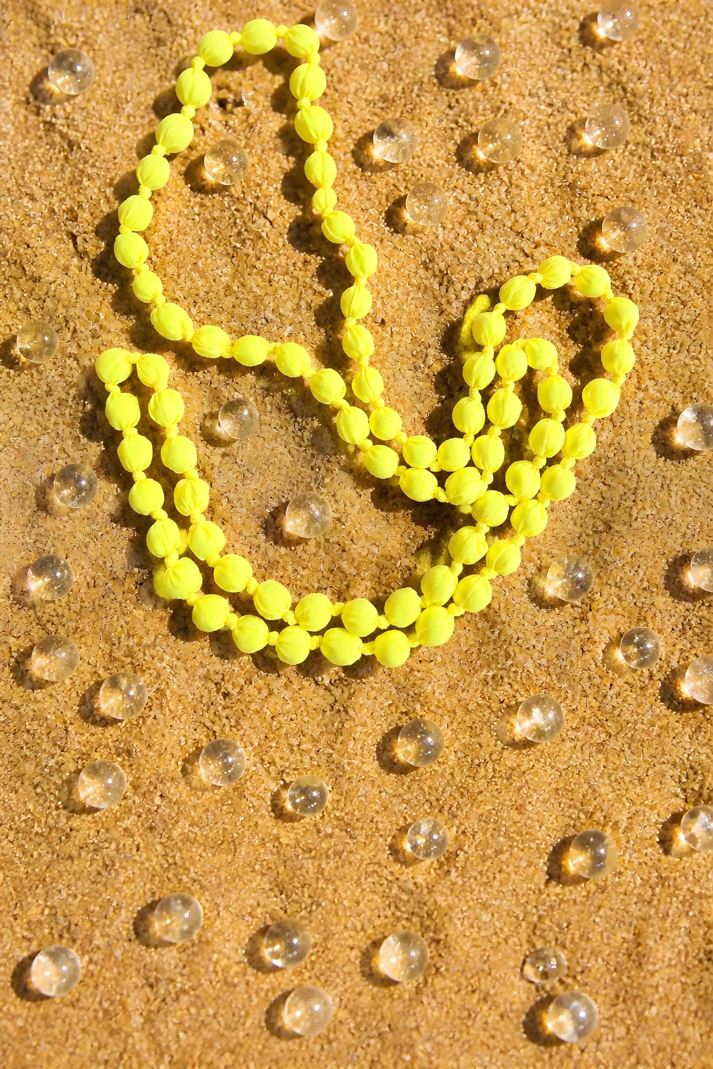 Collar de paño y madera artesanal Begur en color amarillo neón expuesto en un fondo arenoso de EuTea.