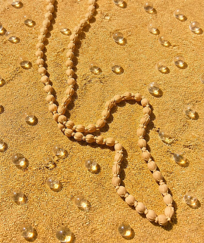 Collar artesanal largo Begur en tono beige arena, elaborado con cuentas de madera y tela suave sobre superficie de arena.