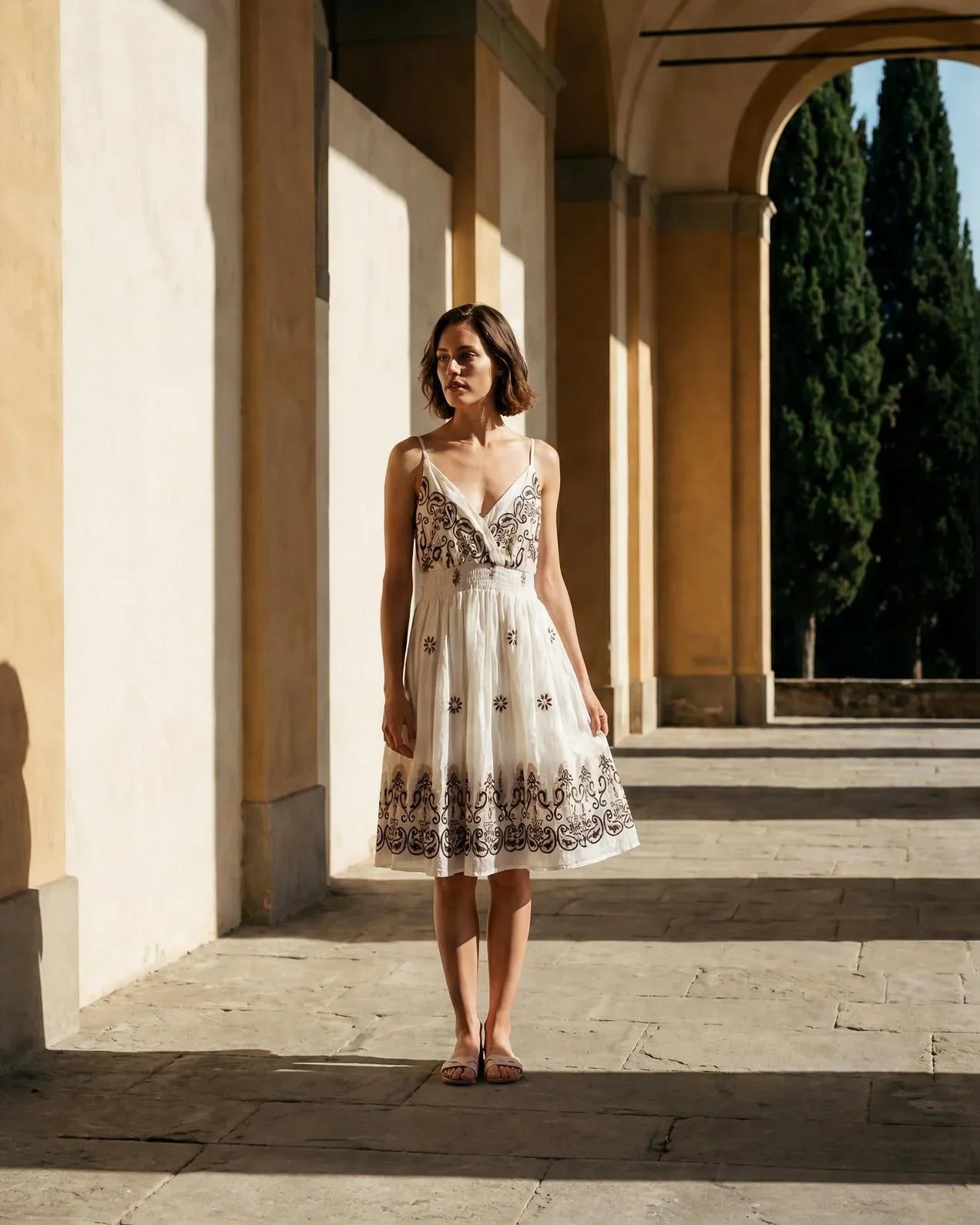Vestido de tirantes Pollenca en color blanco con bordados boho en contraste de la marca EUTEA, posando de frente en un patio soleado