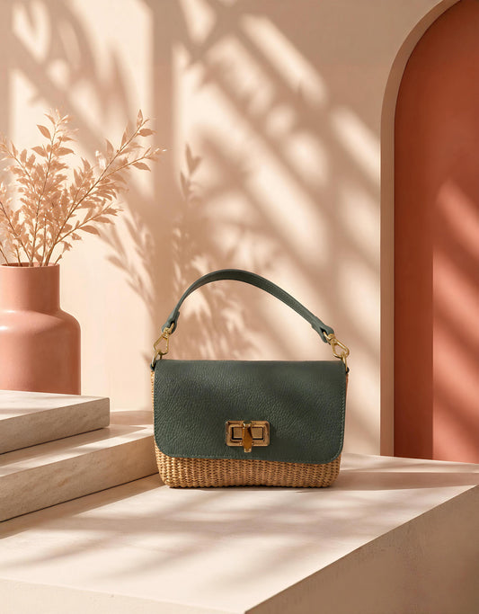 Bolso bimaterial Tárrega de EUTEA en color verde oliva y base de rafia trenzada, con herraje metálico dorado, apoyado sobre una superficie de piedra clara bajo luces y sombras decorativas