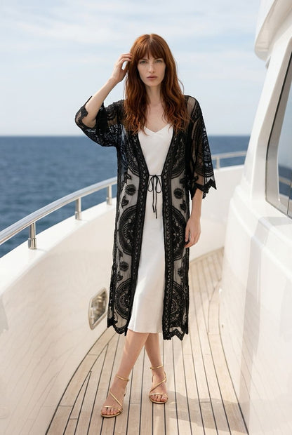 Vista frontal de la modelo con el kimono de encaje negro Segovia de Eutea atado a la cintura sobre un vestido lencero blanco.