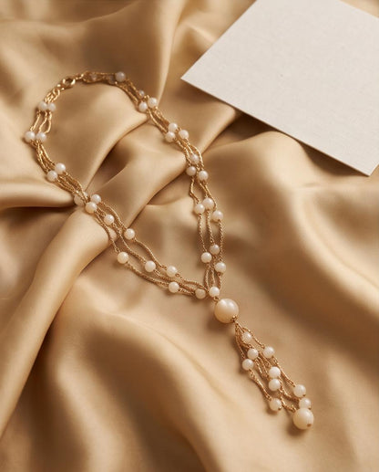 Collar de cuentas blancas y cadenas doradas presentado sobre tejido satinado.