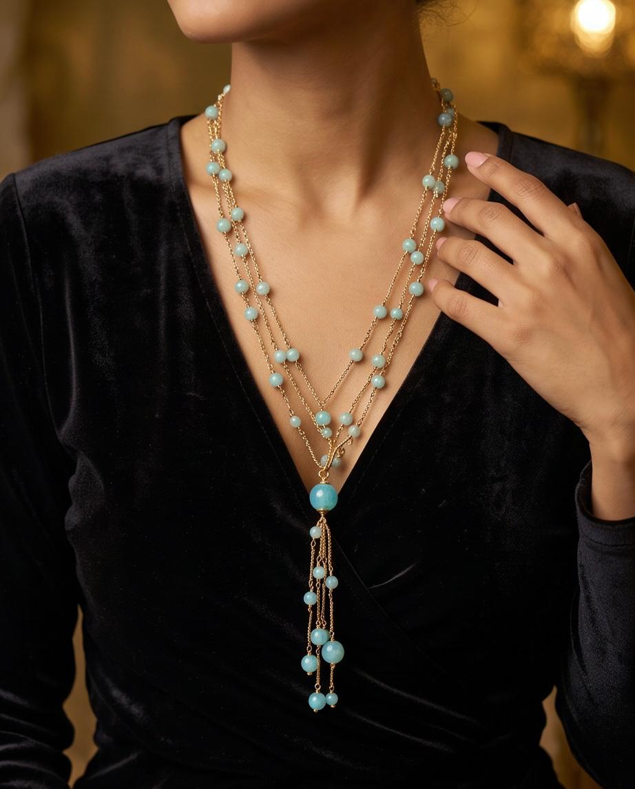 Mujer llevando collar largo dorado con cuentas azul turquesa y caída en cascada.