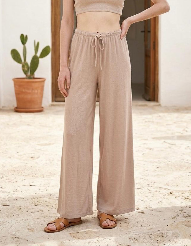 Modelo posando de frente con el pantalón fluido de tiro alto con cordón en color beige arena Livia.