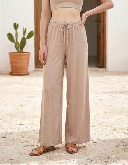 Modelo posando de frente con el pantalón fluido de tiro alto con cordón en color beige arena Livia.