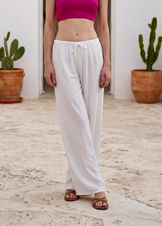 Pantalón palazzo elástico de verano en color blanco combinado con un top corto fucsia en un entorno mediterráneo.