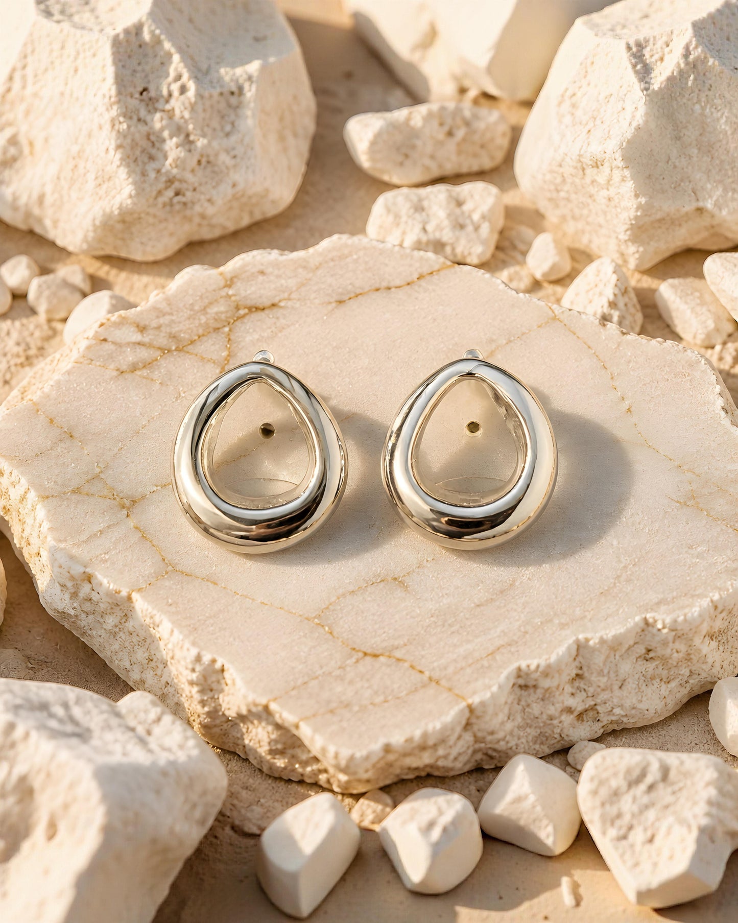 Pendientes plateados de gota Tarragona de EuTea, fabricados en acero inoxidable de diseño fluido e hipoalergénico sobre una roca clara.