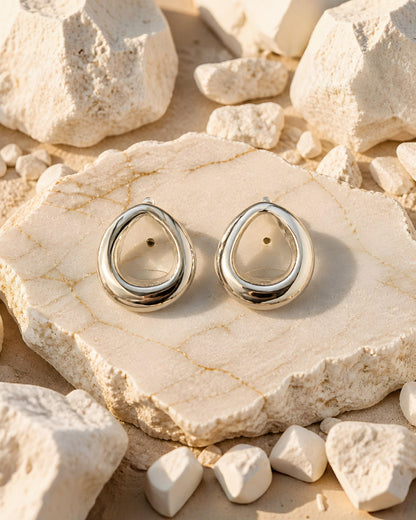 Pendientes plateados de gota Tarragona de EuTea, fabricados en acero inoxidable de diseño fluido e hipoalergénico sobre una roca clara.