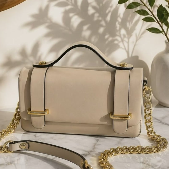 Vista cenital del bolso de mano de cuero rígido modelo Cunit de la marca EUTEA en color camel, mostrando el diseño plano de su asa superior y los acabados metálicos dorados en una mesa iluminada por el sol.
