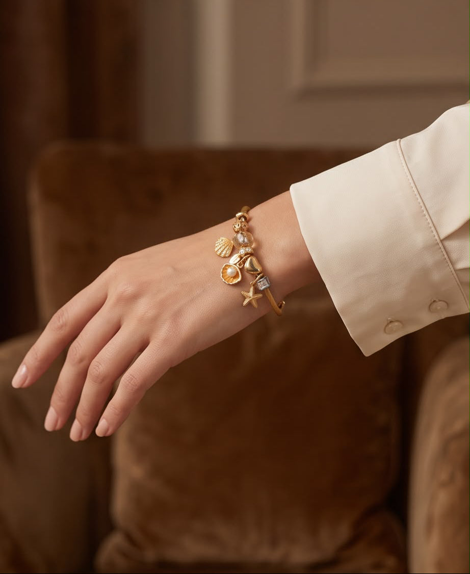 Mujer luciendo la Pulsera Mojácar dorada con charms de concha, perla y estrella de mar de Eutea.