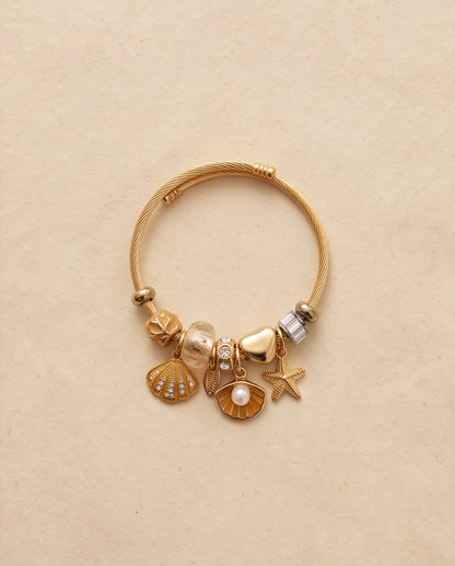 Pulsera Mojácar dorada con charms inspirados en el mar sobre fondo claro.