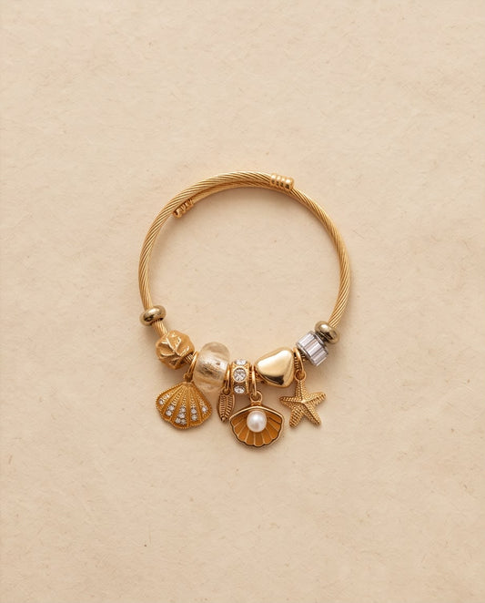 Pulsera Mojácar dorada con charms inspirados en el mar sobre fondo claro.