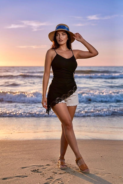 Modelo posando de frente en la playa con top asimétrico negro con encaje Sari y shorts blancos.
