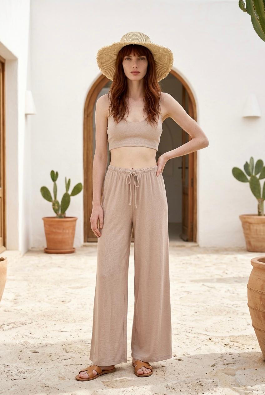 Modelo posando de frente con top corto minimalista de punto texturizado color beige arena con sombrero de paja.