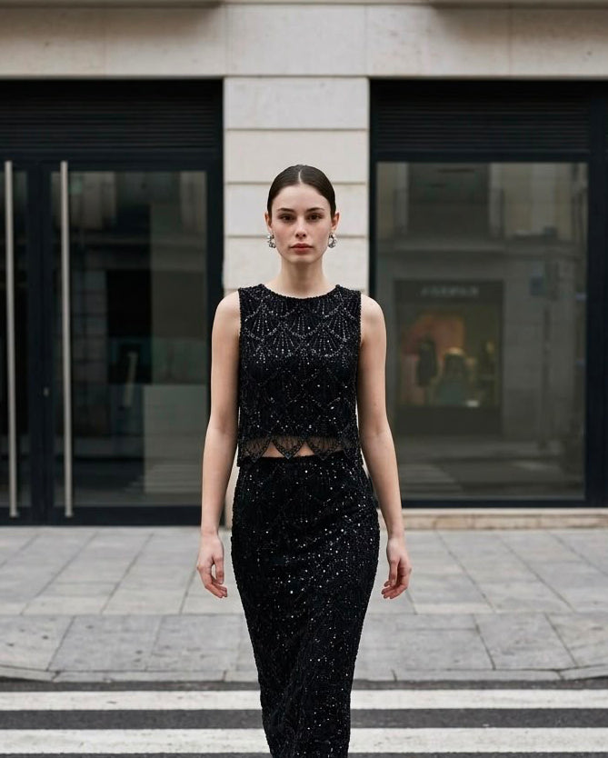 Modelo vistiendo el Top Corto de Pedrería Marconi en color negro de Eutea, combinado con falda midi de lentejuelas en un paso de peatones.