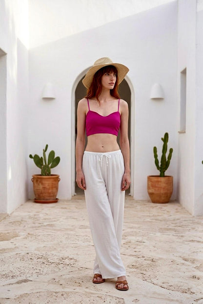 Modelo luciendo un crop top de tirantes finos en color fucsia vibrante combinado con pantalón blanco.