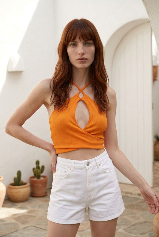 Modelo posando de frente con el top crop halter naranja Álava de Eutea y shorts blancos.
