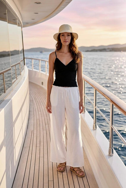 Modelo de frente en la cubierta de un barco con top de tirantes negro en nido de abeja y pantalón blanco fluido.