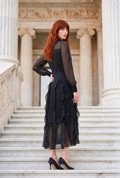 Plano de perfil de la modelo mostrando la caída de los volantes traseros y la manga larga semitransparente del Vestido Aduana negro.